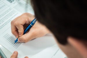 Leitor de gabarito. Aluno com mão segurando caneta e preenchendo gabarito de respostas na mesa.